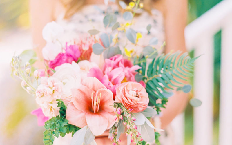 Color-filled bridesmaid bouquet included  bold coral ranunculus, pink peonies, peach stargazer lilies, bougainvillea, yellow leaves, eucalyptus, greenery, orange tulips and blush ranunculus wrapped in silk ribbon