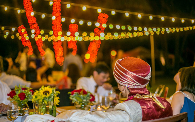 Red rose and sunflower centerpieces lit by string lights create ambiance at waterfront wedding reception